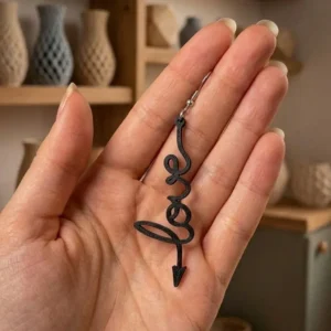 Boucles d'oreilles Love noires en impression 3D tenues dans la main pour montrer la taille.