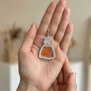 Paire de boucles d'oreilles poisson rouge en sachet tenue en main pour montrer la taille réelle.