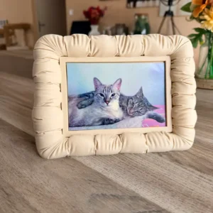 Cadre photo design effet matelassé boudin couleur sable beige, imprimé en 3D, posé sur une table en bois avec une photo de deux chats à l'intérieur.