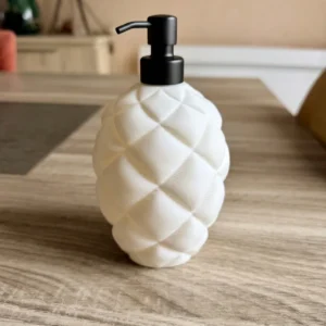 Distributeur de savon liquide blanc mat au motif matelassé puffy, modèle Classique Ovale avec pompe noire, posé sur une table en bois.