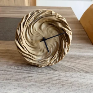 Horloge originale Plissé aspect bois clair avec cadran effet tissu drapé posée sur une table