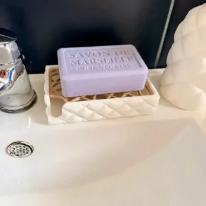 Porte-savon matelassé blanc mat avec grille couleur bois et un savon de Marseille lavande posé sur un lavabo moderne.