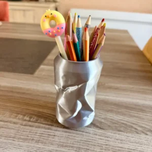 Pot à crayons original argenté en forme de canette de soda écrasée rempli de stylos sur un bureau