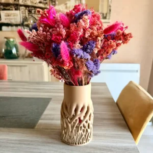 Vase ajouré de couleur sable au design organique inspiré de racines entrelacées, imprimé en 3D, contenant un grand bouquet de fleurs séchées sur une table.